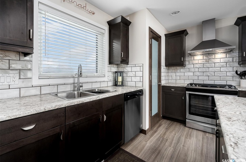 Kitchen with sink, light hardwood / wood-style floors, stainless steel appliances, wall chimney range hood, and backsplash