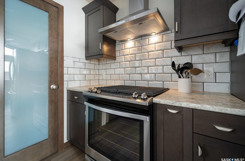 Kitchen with tasteful backsplash, wall chimney exhaust hood, stainless steel range with gas cooktop, and light stone countertops