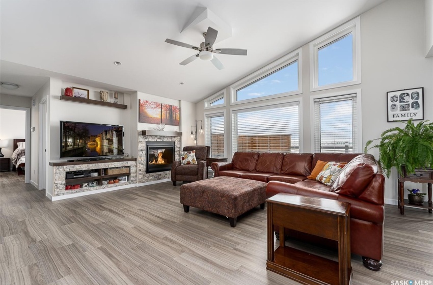 Living room with ceiling fan, high vaulted ceiling, a wealth of natural light, light hardwood / wood-style floors, and a stone fireplace