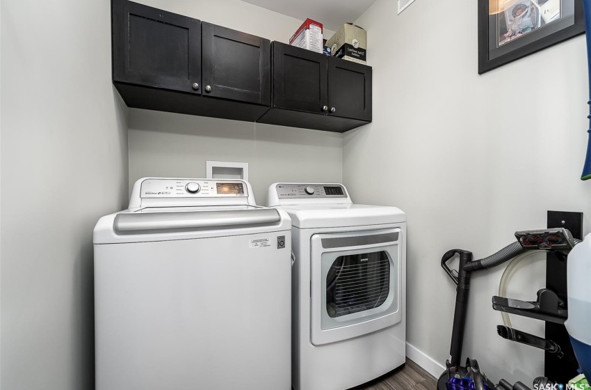 Clothes washing area with dark hardwood / wood-style flooring, washer and clothes dryer, cabinets, and hookup for a washing machine