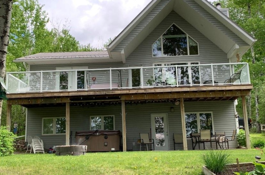 Back of property featuring a balcony, a lawn, and a hot tub