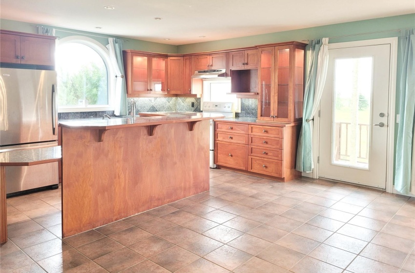 Kitchen featuring a kitchen breakfast bar, white electric range oven, light tile flooring, tasteful backsplash, and stainless steel refrigerator