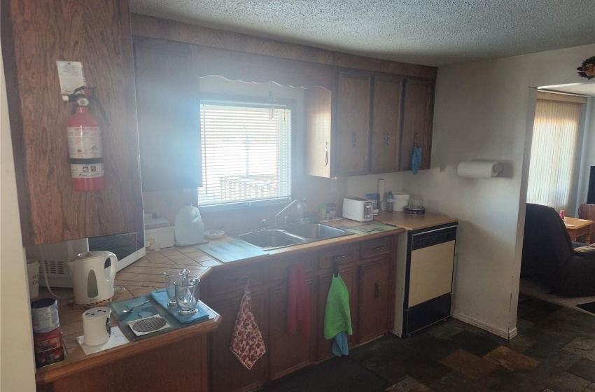 Kitchen with dark tile floors, a textured ceiling, stainless steel dishwasher, and sink