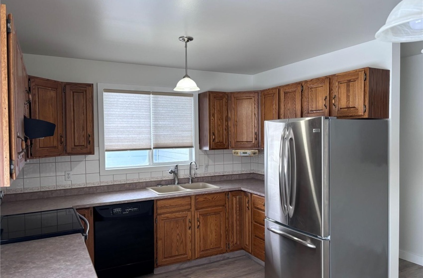 Kitchen with dishwasher, dark hardwood / wood-style flooring, stainless steel fridge, sink, and backsplash