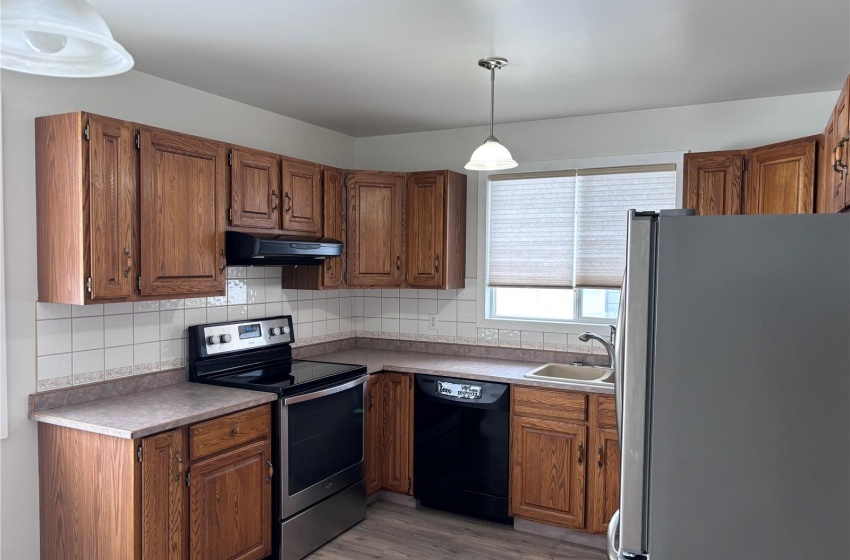 Kitchen featuring ventilation hood, light wood-type flooring, hanging light fixtures, sink, and appliances with stainless steel finishes