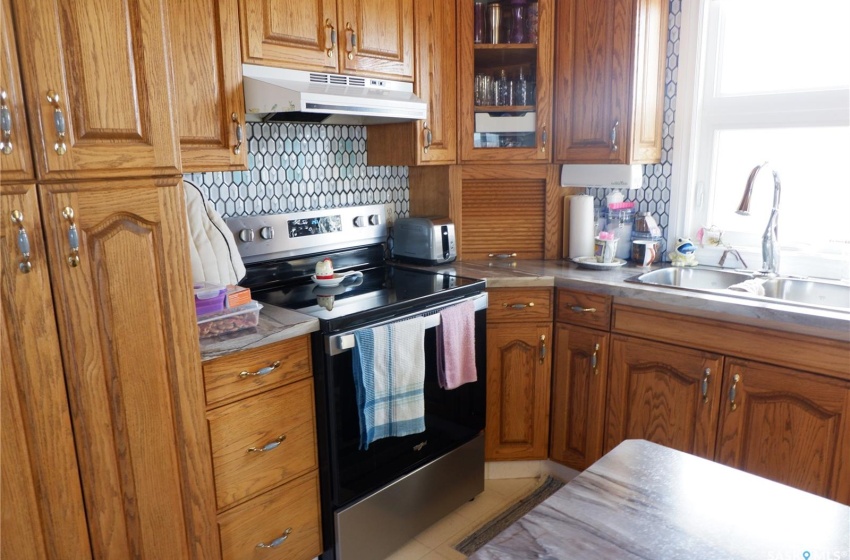 Kitchen with backsplash, stainless steel electric stove, sink, and light tile floors