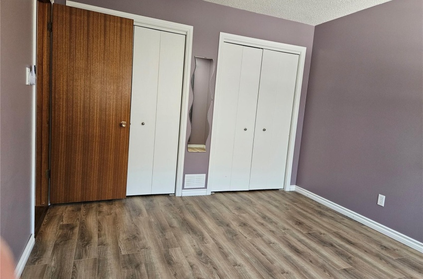 Unfurnished bedroom with a textured ceiling, dark hardwood / wood-style flooring, and two closets