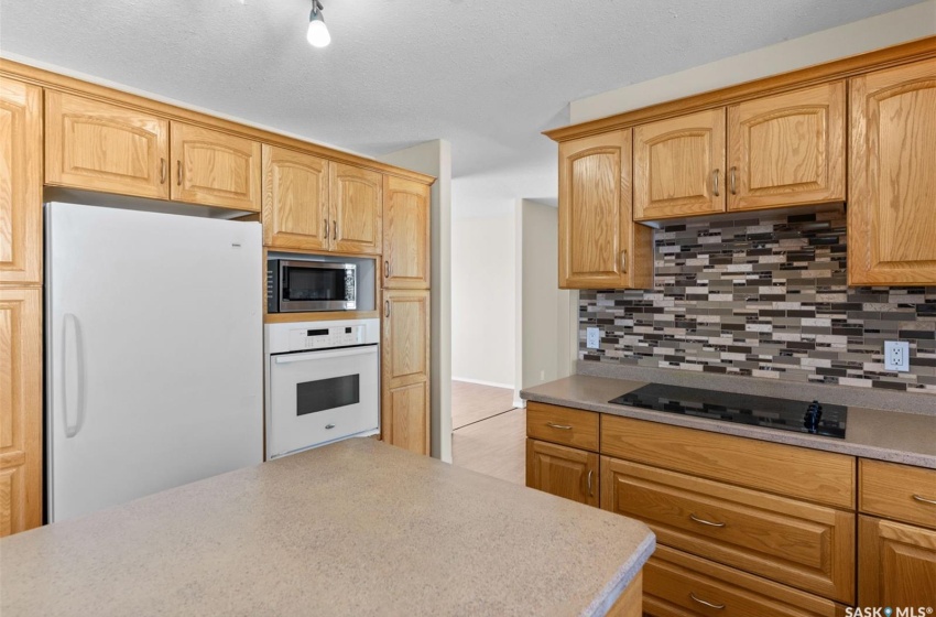 Kitchen featuring backsplash, white appliances, a textured ceiling, and track lighting