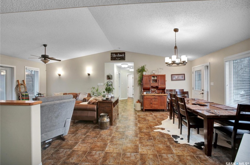 Living room with a textured ceiling, vaulted ceiling, dark tile floors, and ceiling fan with notable chandelier