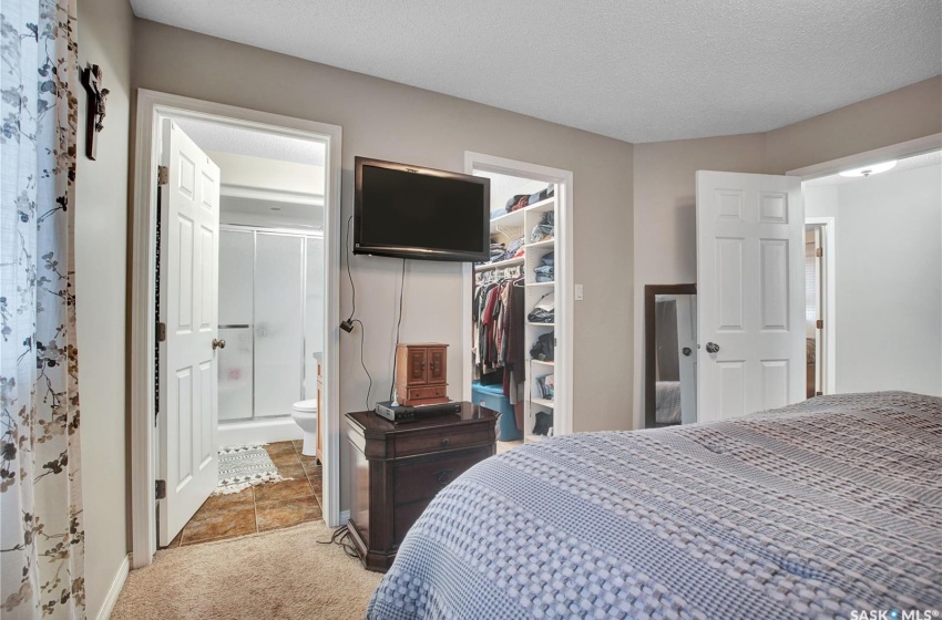 Bedroom with a spacious closet, ensuite bath, light carpet, a closet, and a textured ceiling