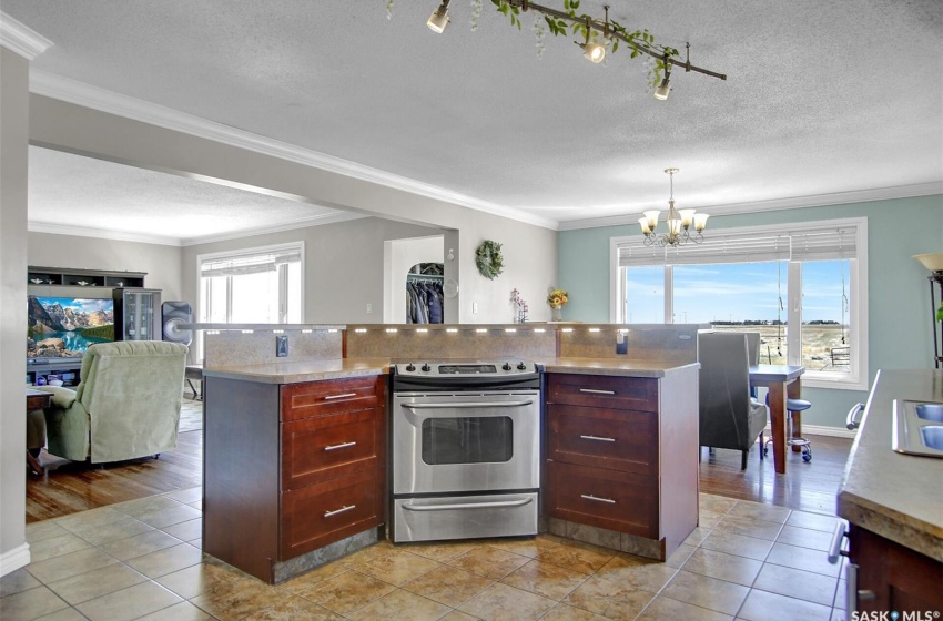 Kitchen with stainless steel range with electric stovetop, crown molding, backsplash, an inviting chandelier, and light tile floors