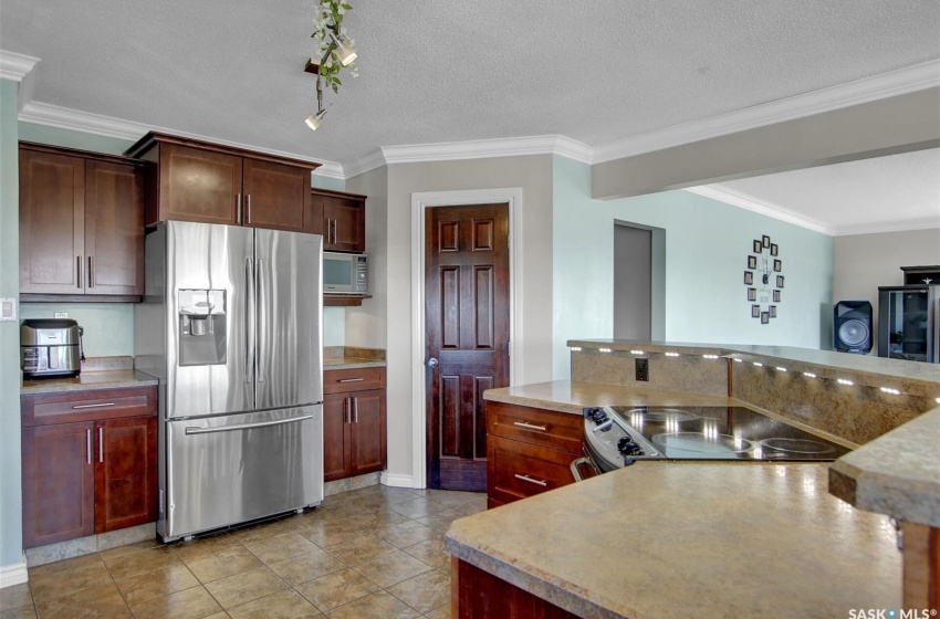 Kitchen with a textured ceiling, stainless steel appliances, light tile floors, and ornamental molding