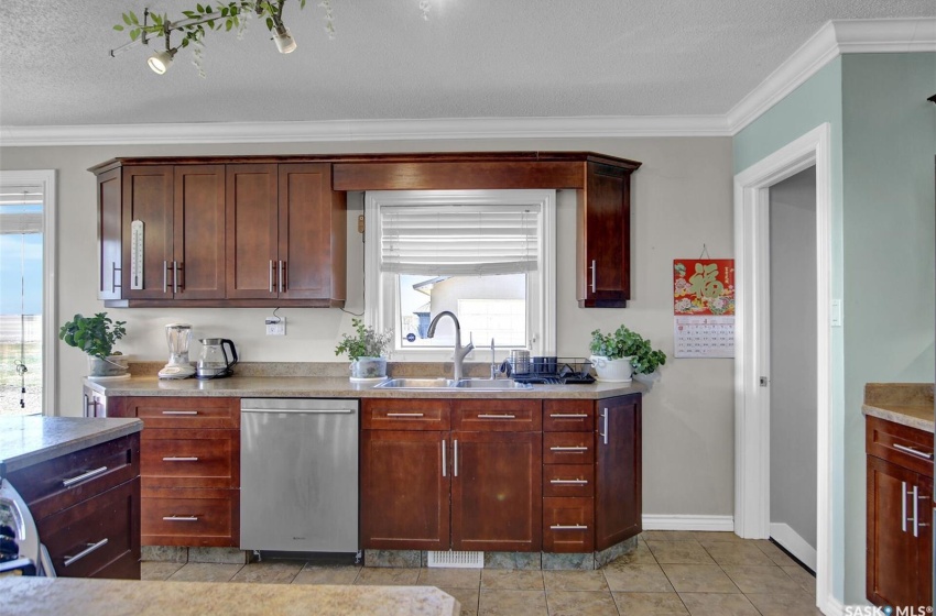 Kitchen featuring ornamental molding, sink, light tile floors, stainless steel dishwasher, and a textured ceiling