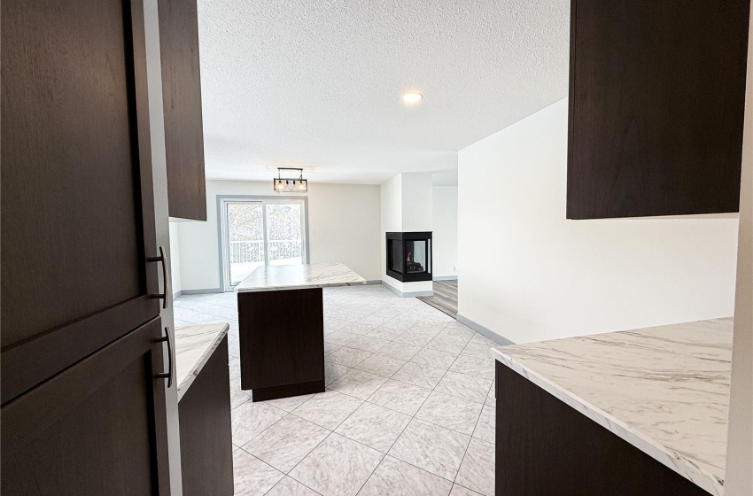 Kitchen featuring a multi sided fireplace, dark brown cabinetry, a center island, and a textured ceiling