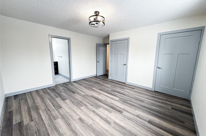 Unfurnished bedroom with a textured ceiling, connected bathroom, and light hardwood / wood-style floors