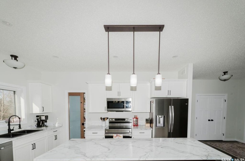 Kitchen featuring sink, white cabinets, decorative light fixtures, appliances with stainless steel finishes, and light stone counters