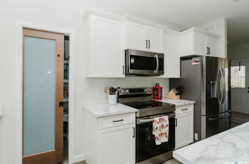 Kitchen featuring light wood-type flooring, a textured ceiling, white cabinetry, stainless steel appliances, and light stone counters