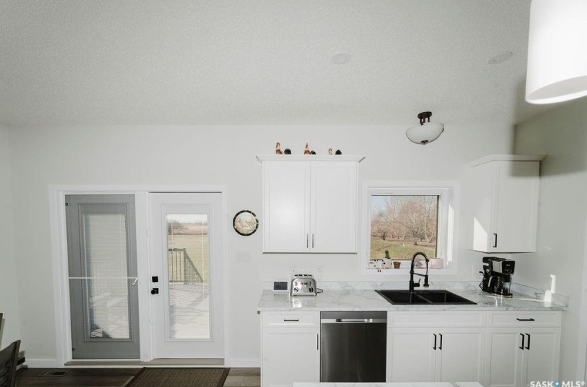 Kitchen with stainless steel dishwasher, sink, white cabinets, and light stone countertops