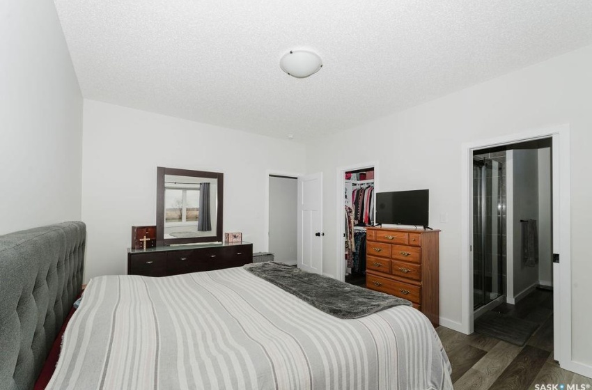 Bedroom with a spacious closet, ensuite bath, a textured ceiling, a closet, and dark wood-type flooring