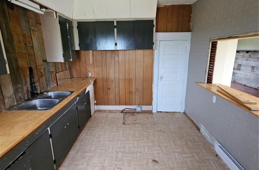 Kitchen with wood walls, a textured ceiling, a baseboard heating unit, and light parquet flooring