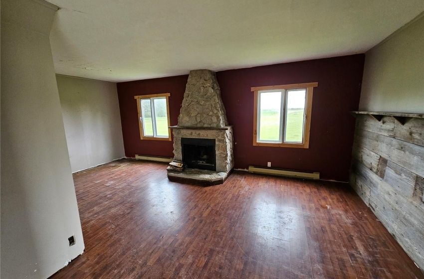 Unfurnished living room featuring a stone fireplace, dark wood-type flooring, plenty of natural light, and a baseboard heating unit