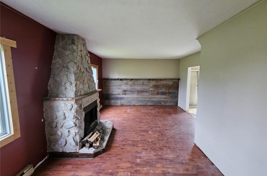 Unfurnished living room featuring a stone fireplace, plenty of natural light, a baseboard radiator, and wood-type flooring