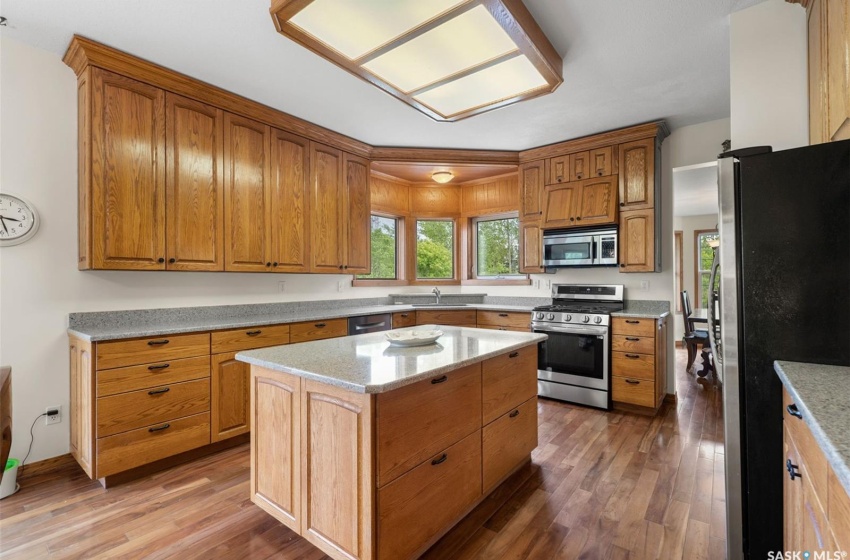 Kitchen featuring a kitchen island, stainless steel appliances, light stone countertops, wood-type flooring, and sink