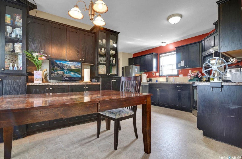 Kitchen featuring dark brown cabinetry, light stone counters, light tile flooring, hanging light fixtures, and appliances with stainless steel finishes