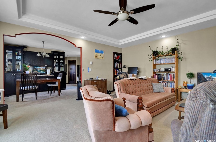 Living room with ceiling fan with notable chandelier, a tray ceiling, and light carpet