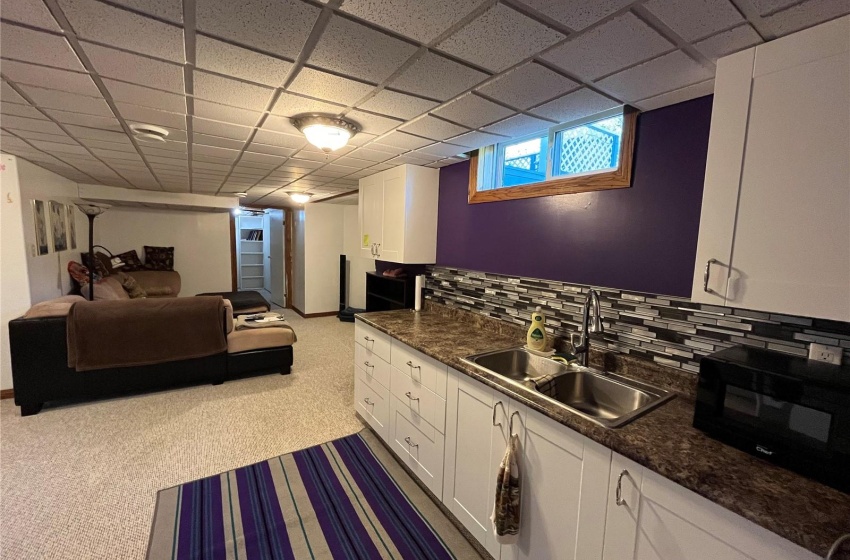 Kitchen with light carpet, sink, decorative backsplash, white cabinets, and a drop ceiling