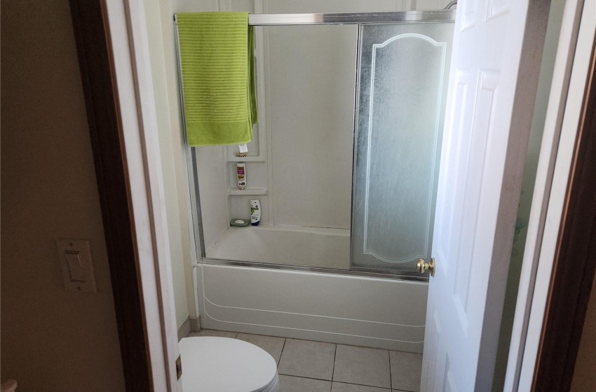 Bathroom with bath / shower combo with glass door, toilet, and tile floors