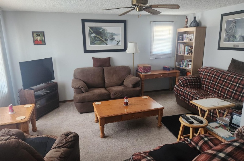 Living room with a textured ceiling, ceiling fan, and dark carpet