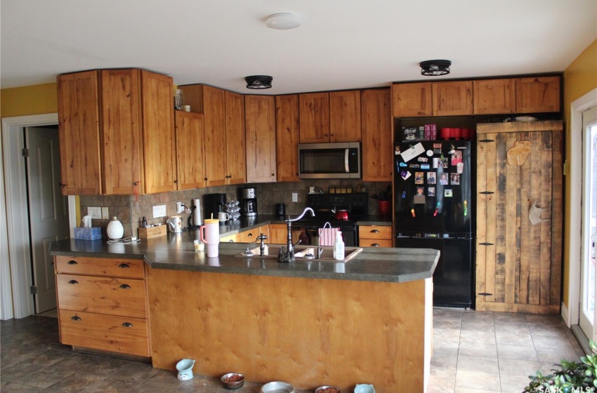 Kitchen with decorative backsplash, black appliances, kitchen peninsula, and sink