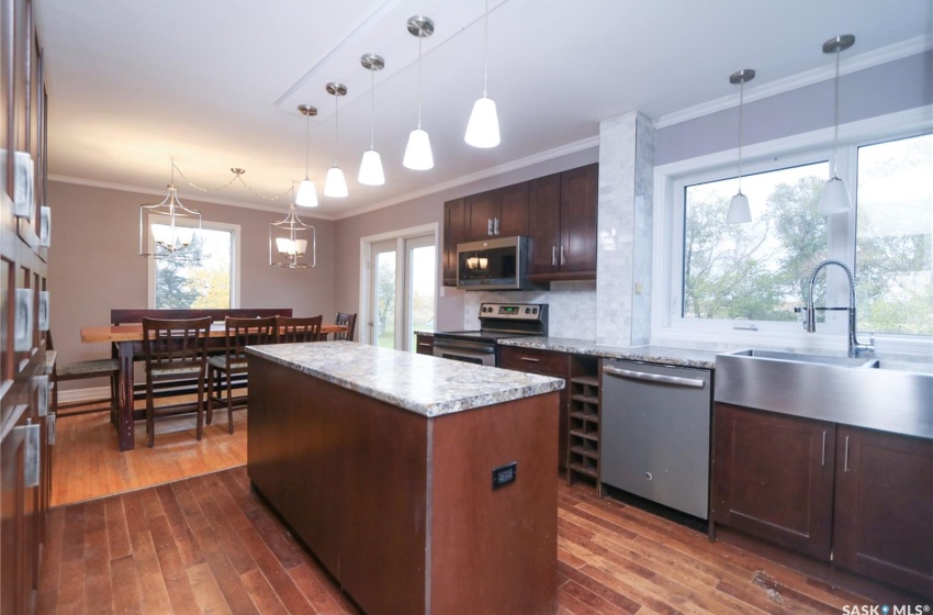 Kitchen featuring stainless steel appliances, hanging light fixtures, crown molding, and dark wood-type flooring