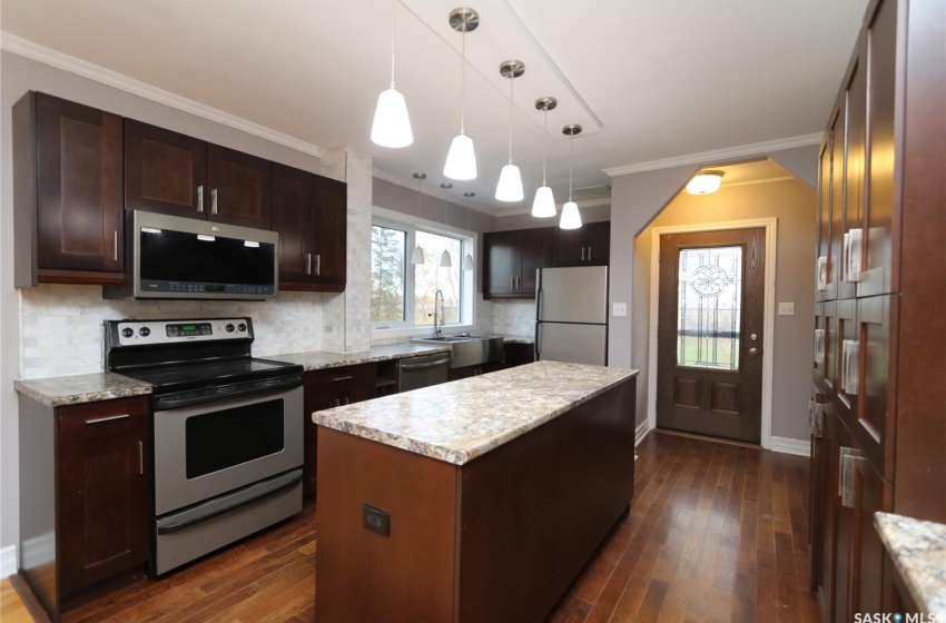 Kitchen with a center island, ornamental molding, dark hardwood / wood-style flooring, pendant lighting, and appliances with stainless steel finishes