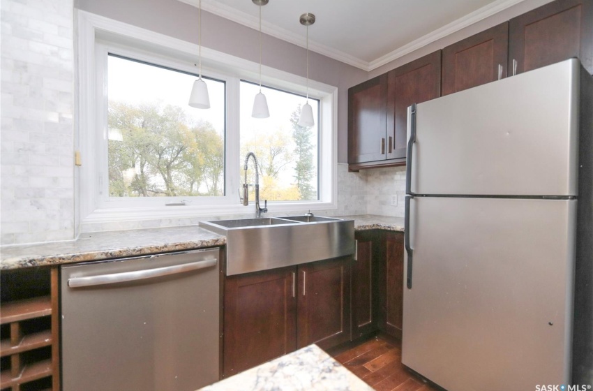 Kitchen with light stone countertops, stainless steel dishwasher, dark wood-type flooring, sink, and white refrigerator