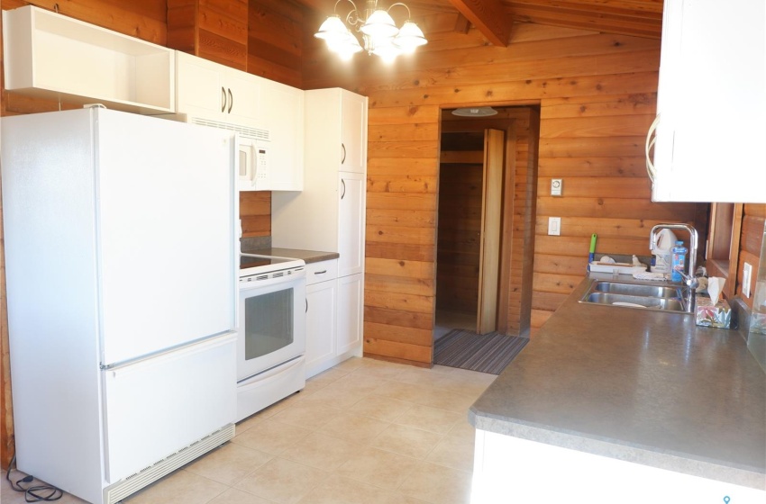 Kitchen with white appliances, white cabinetry, sink, and wooden walls