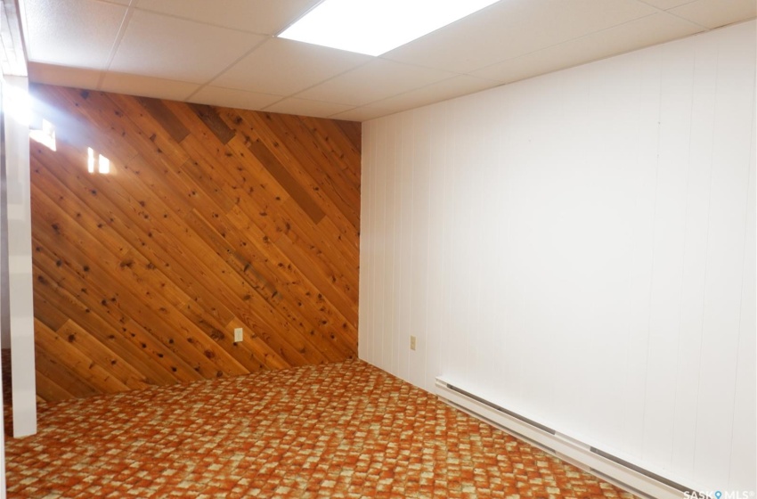 Empty room featuring baseboard heating, a paneled ceiling, and wood walls