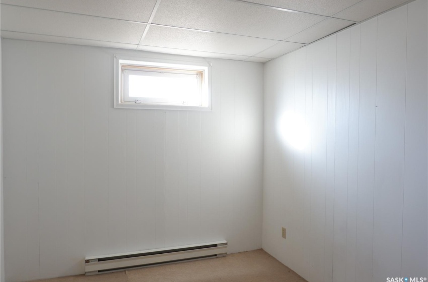 Empty room featuring a drop ceiling, light colored carpet, and a baseboard heating unit