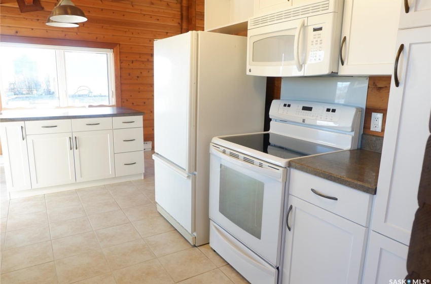 Kitchen with white cabinets, wood walls, light tile patterned floors, and white appliances