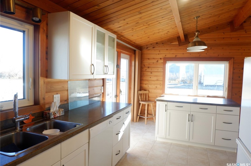 Kitchen featuring white dishwasher, sink, white cabinetry, lofted ceiling with beams, and decorative light fixtures