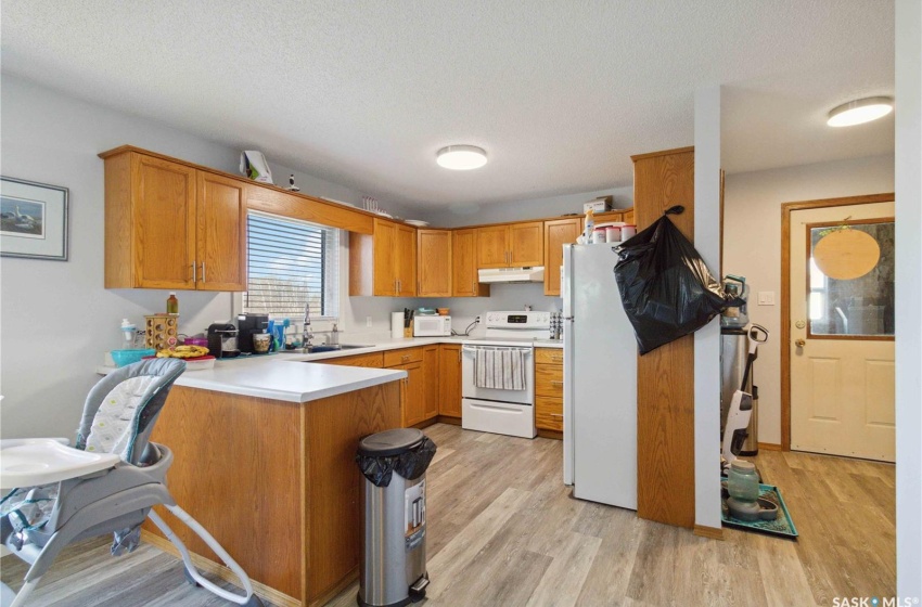 Kitchen with light vinyl plank flooring, kitchen peninsula, a textured ceiling, sink, and white appliances