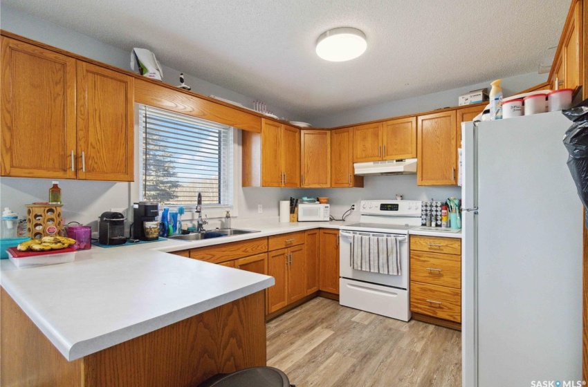 Kitchen with a textured ceiling, white appliances, sink, kitchen peninsula, and vinyl plank flooring