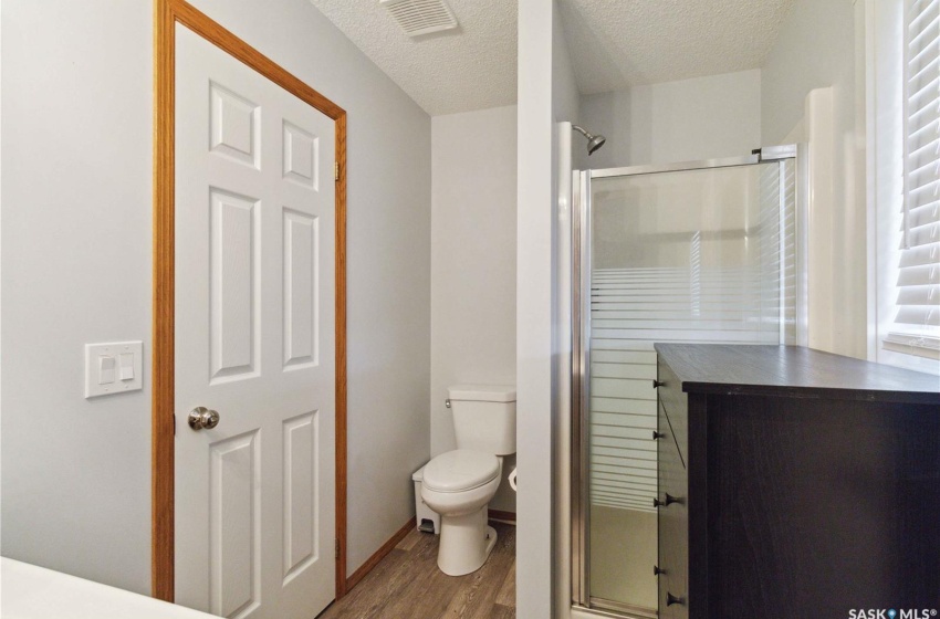 Bathroom featuring vinyl plankfloors, a textured ceiling, toilet, and a shower with door