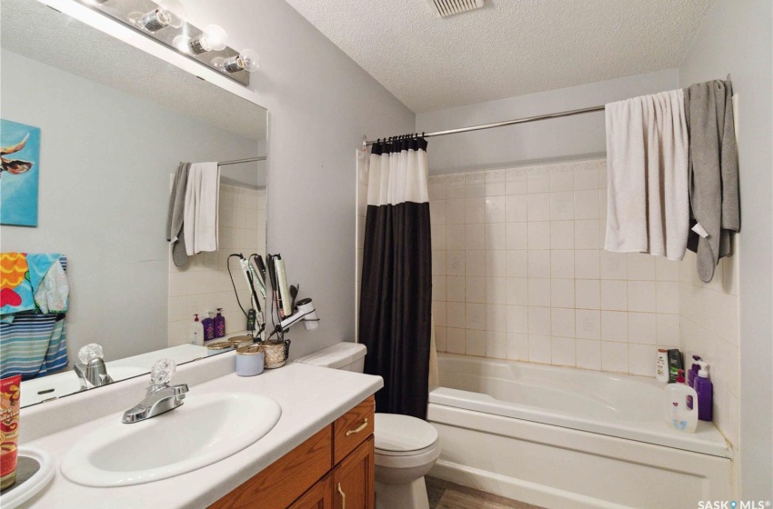 Full bathroom featuring a textured ceiling, shower / bathtub combination with curtain, vinyl plank floors, vanity, and toilet