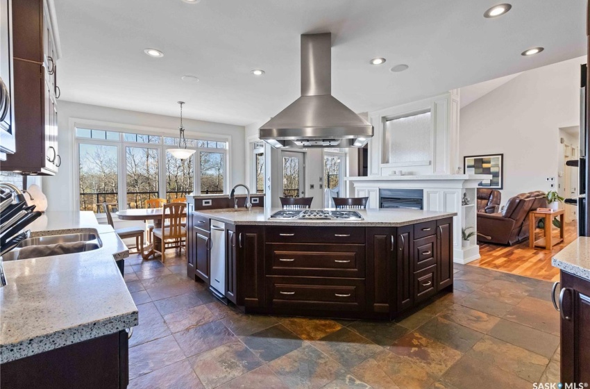 Kitchen featuring dark brown cabinetry, stainless steel gas cooktop, a kitchen island with sink, pendant lighting, and range hood