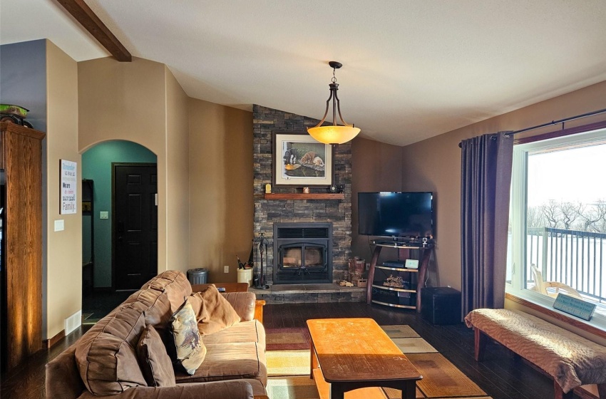 Living room featuring vaulted ceiling with beams, a stone fireplace, and dark hardwood / wood-style floors