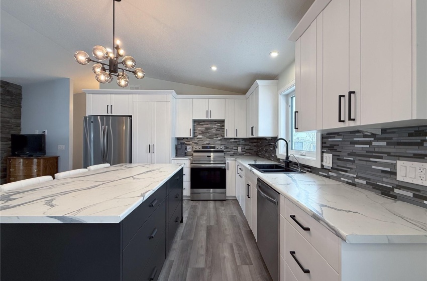 Kitchen with appliances with stainless steel finishes, white cabinetry, sink, hanging light fixtures, and a center island