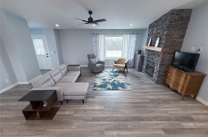 Living room with wood-type flooring, a stone fireplace, and ceiling fan