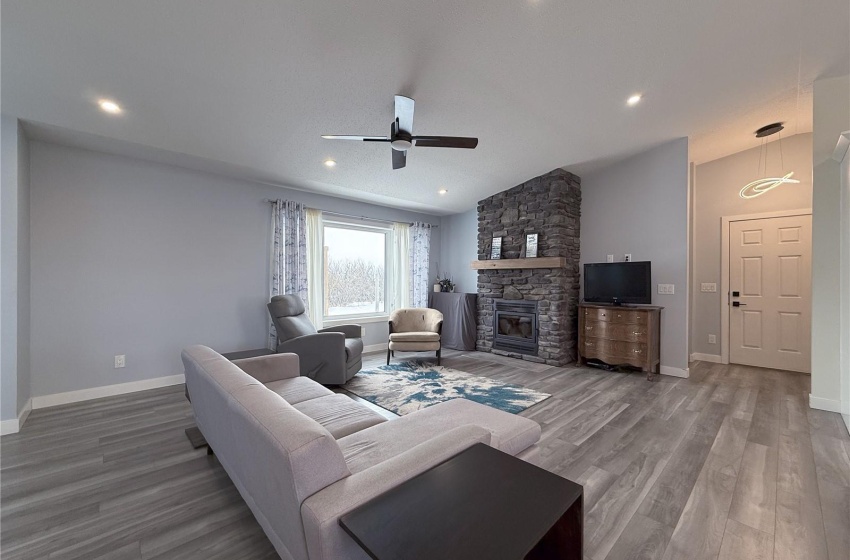 Living room with ceiling fan, wood-type flooring, a stone fireplace, and vaulted ceiling